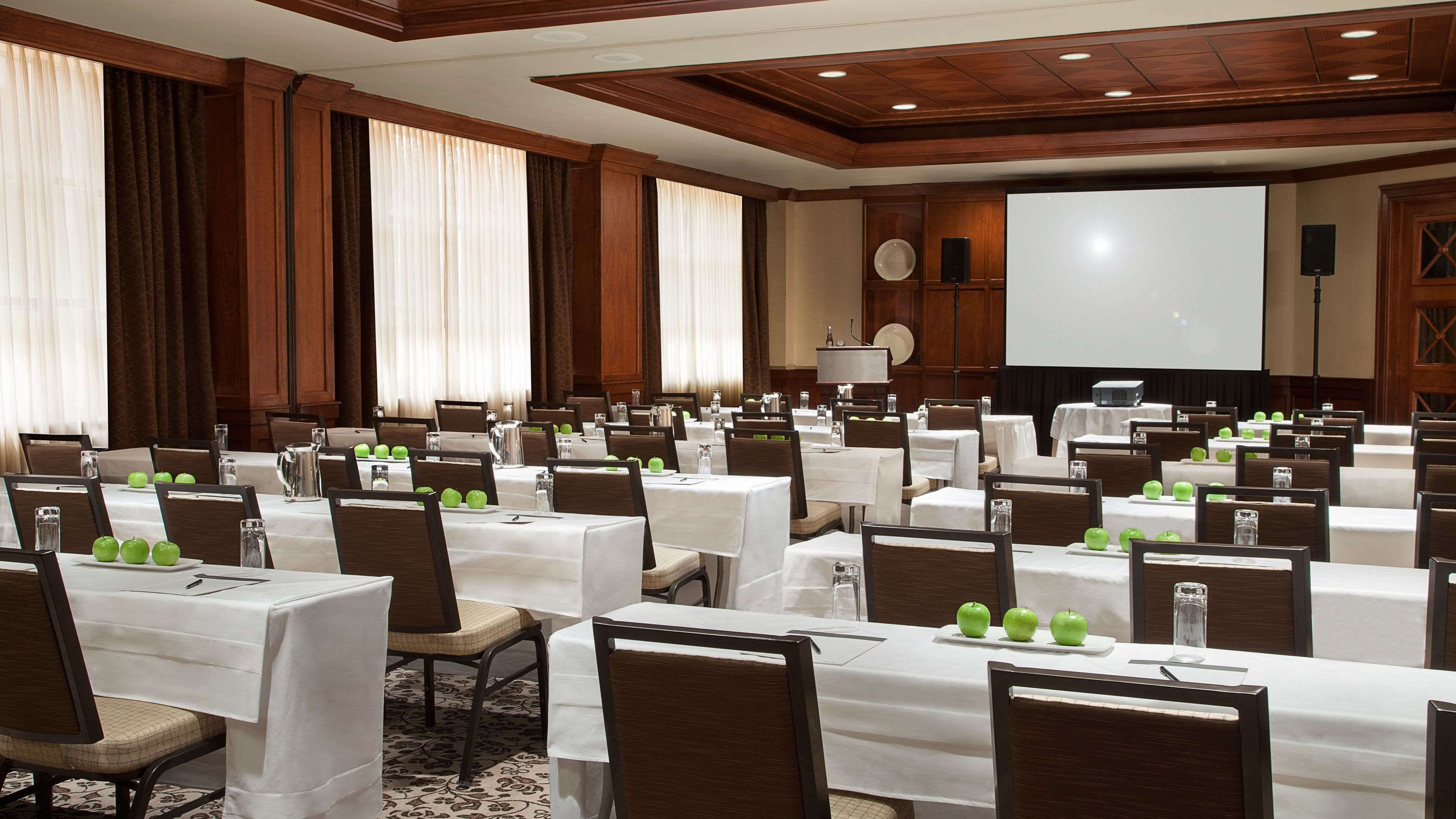A conference room with multiple tables, chairs, and a large screen.