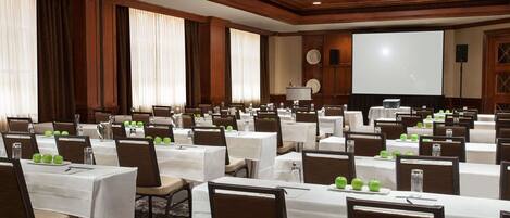 A conference room with multiple tables, chairs, and a large screen.