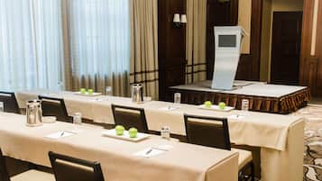 Un salón de conferencias con una larga mesa, sillas, un atril y una pantalla de proyector.