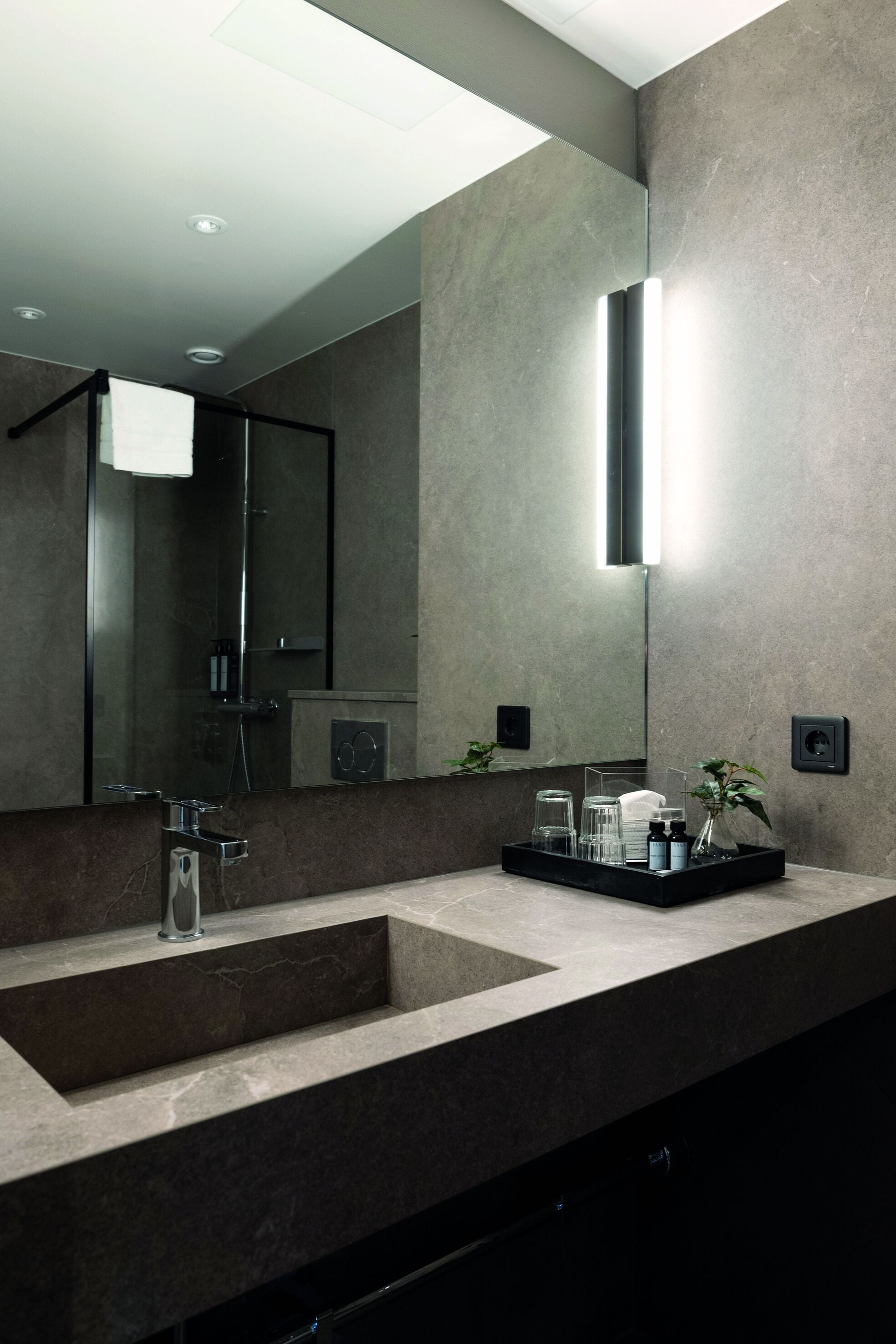 A modern bathroom with a large mirror, a sink, and a tray with toiletries.