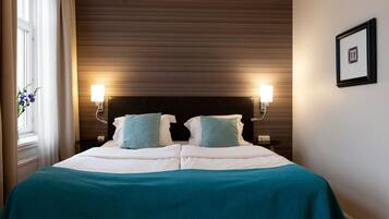 Una habitación de hotel con una cama, dos lámparas de noche, un cuadro en la pared y una ventana con cortinas.
