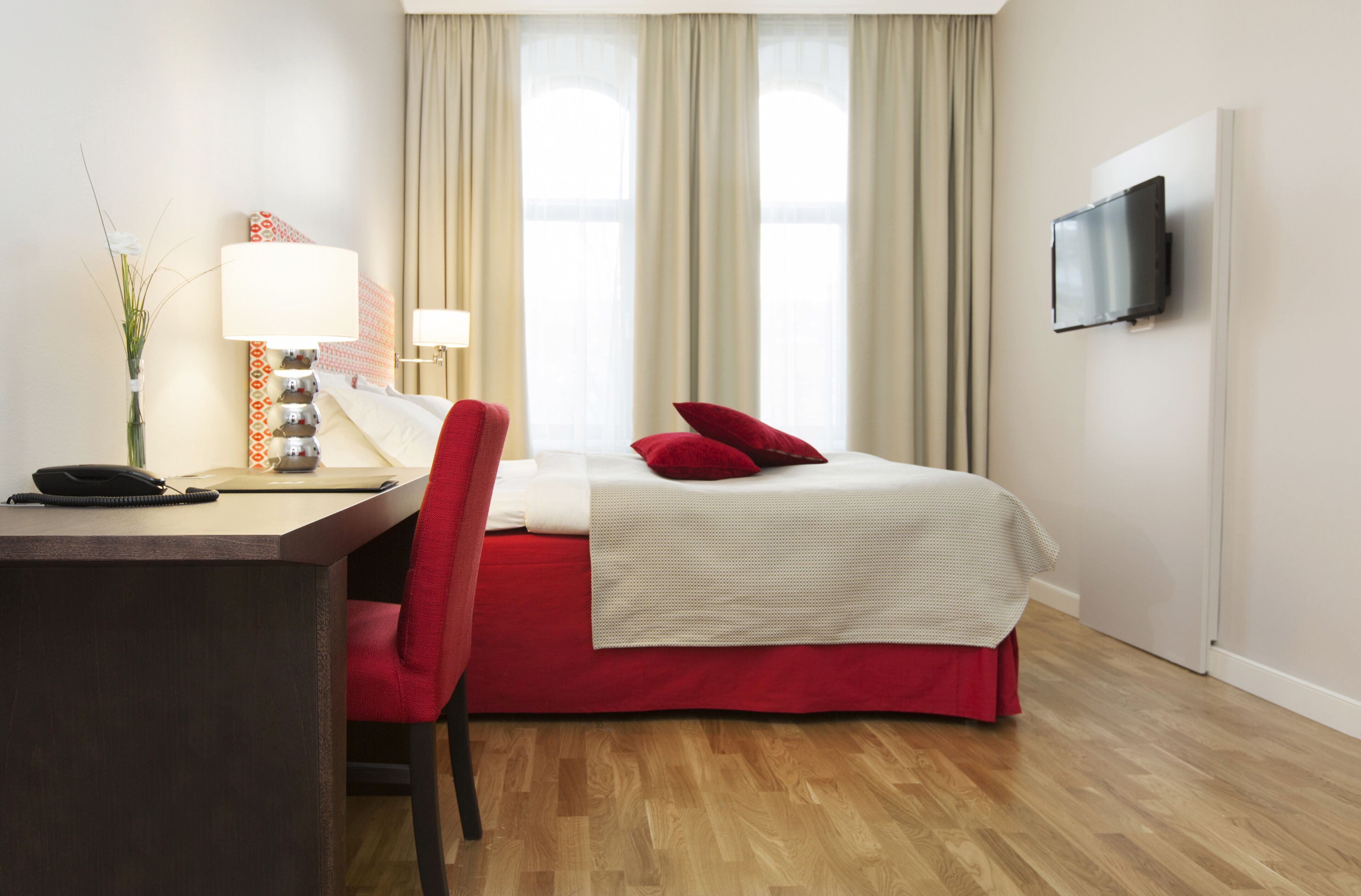 A hotel room with a bed, a desk, a chair, a TV, and a window with curtains.