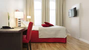 A hotel room with a bed, a desk, a chair, a TV, and a window with curtains.