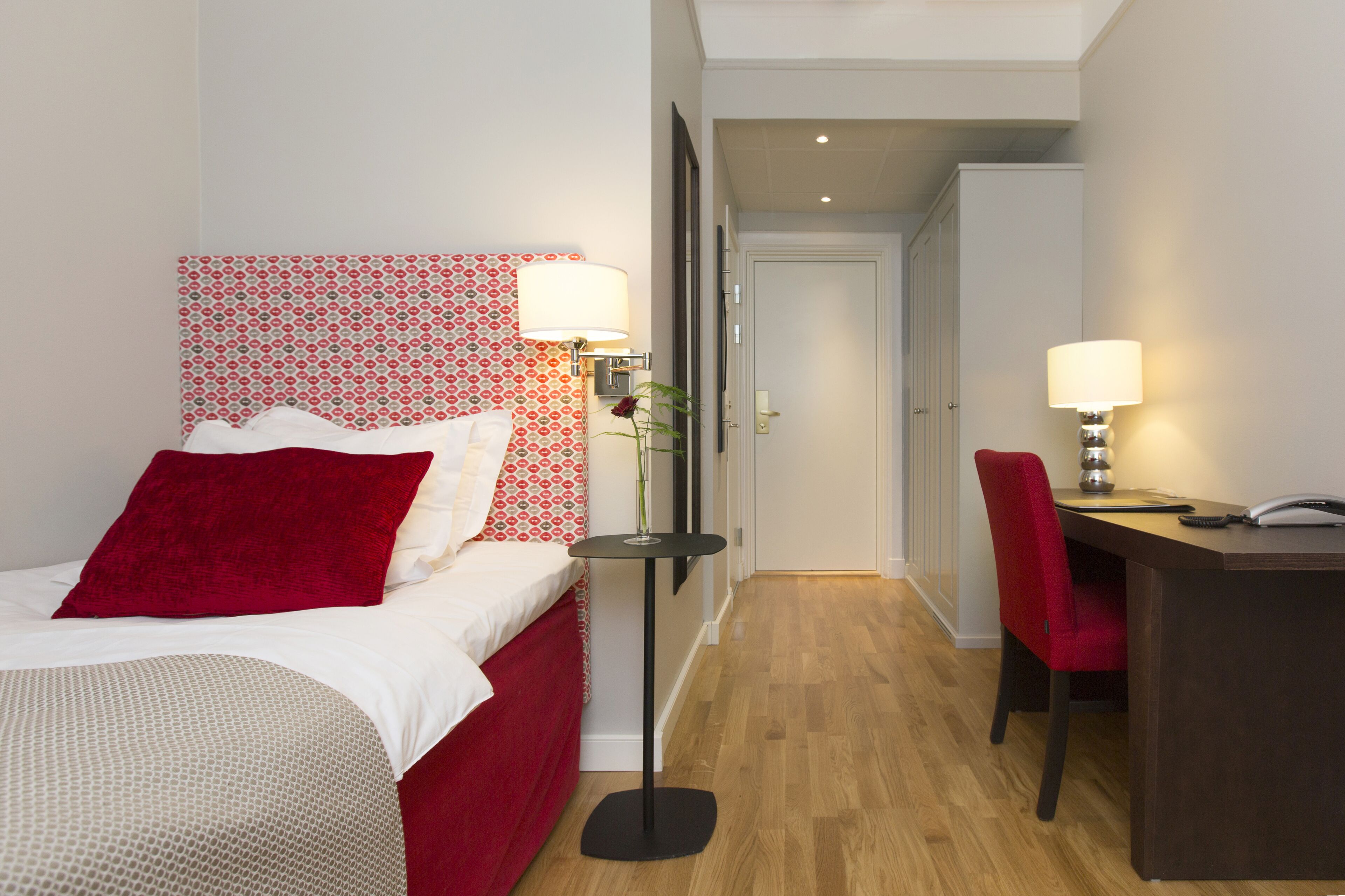 A hotel room with a bed, a desk, a chair, and a door leading to another room.