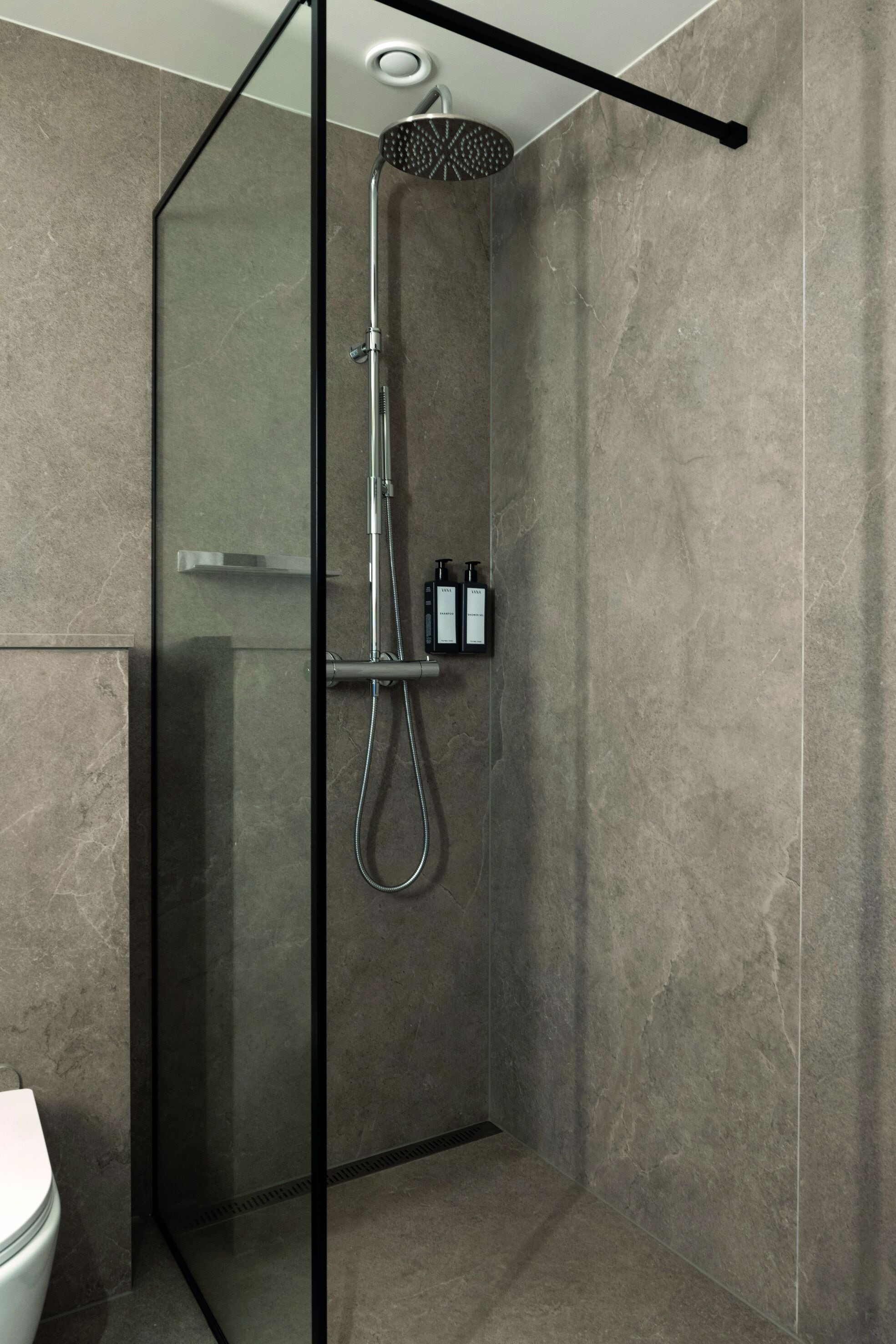Un box de ducha moderno con puerta de vidrio, ducha de mano y panel de control en la pared.