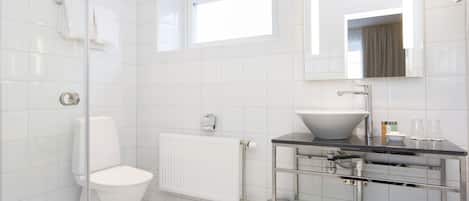 A modern bathroom with a white toilet, a glass shower enclosure, a white sink, and a mirror above the sink.