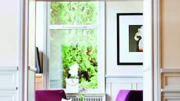 Ein Zimmer mit Blick durch ein Fenster, ausgestattet mit einem violetten Sofa und einem kleinen Tisch mit einer Vase.
