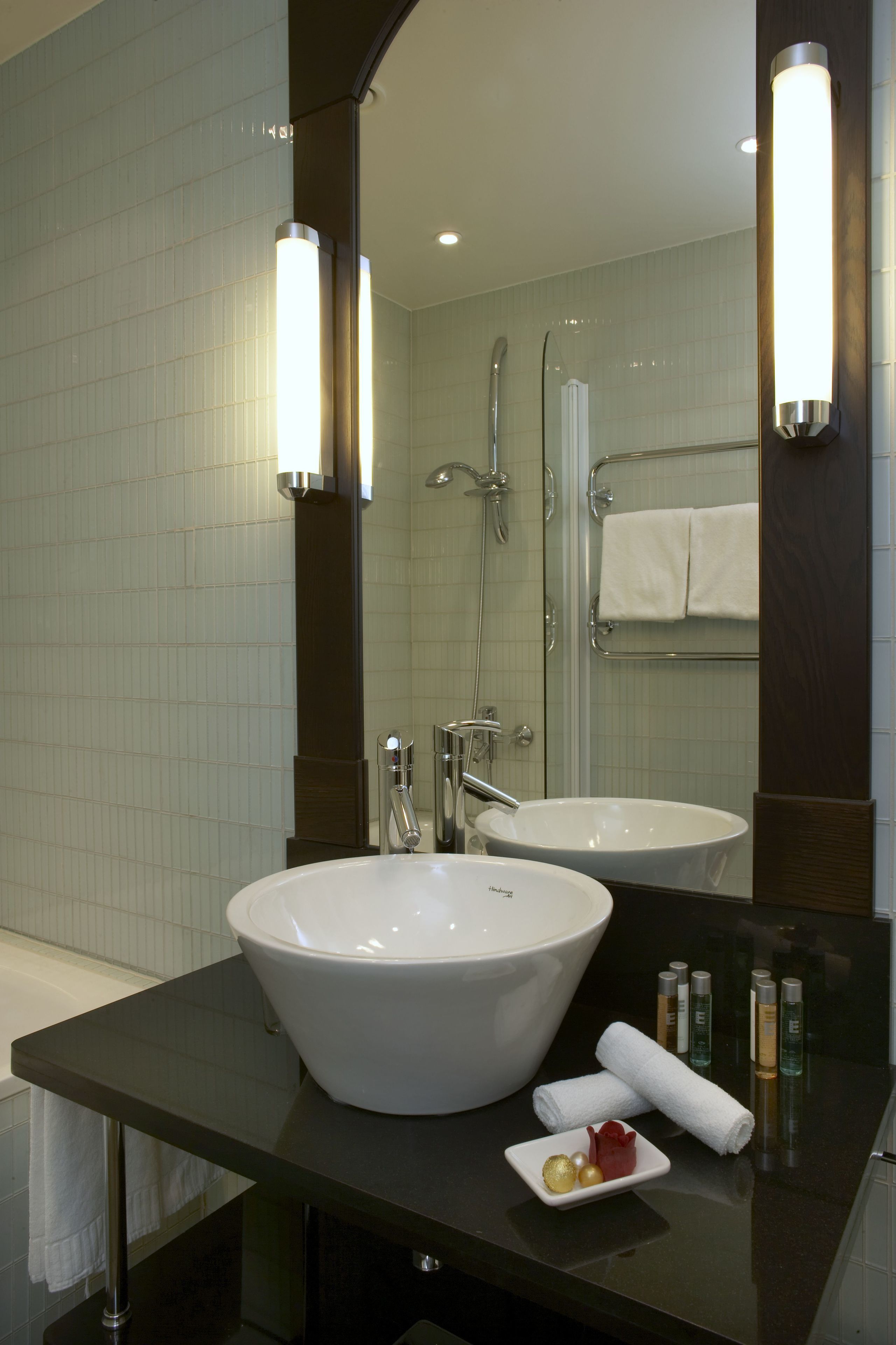 A modern bathroom with a large white sink, a mirror, and a shower.