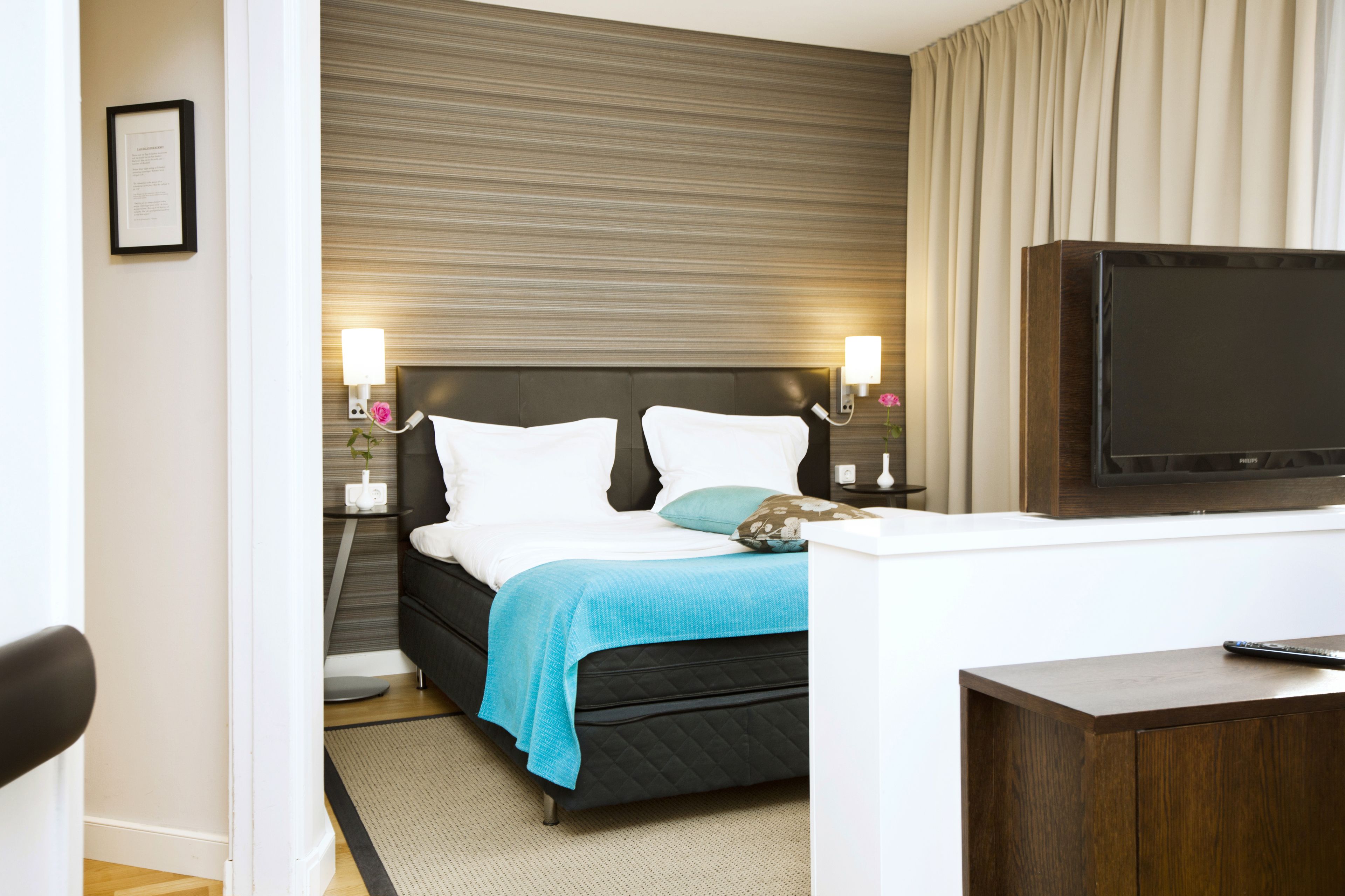 A hotel room with a bed, bedside lamps, a TV, and a desk.