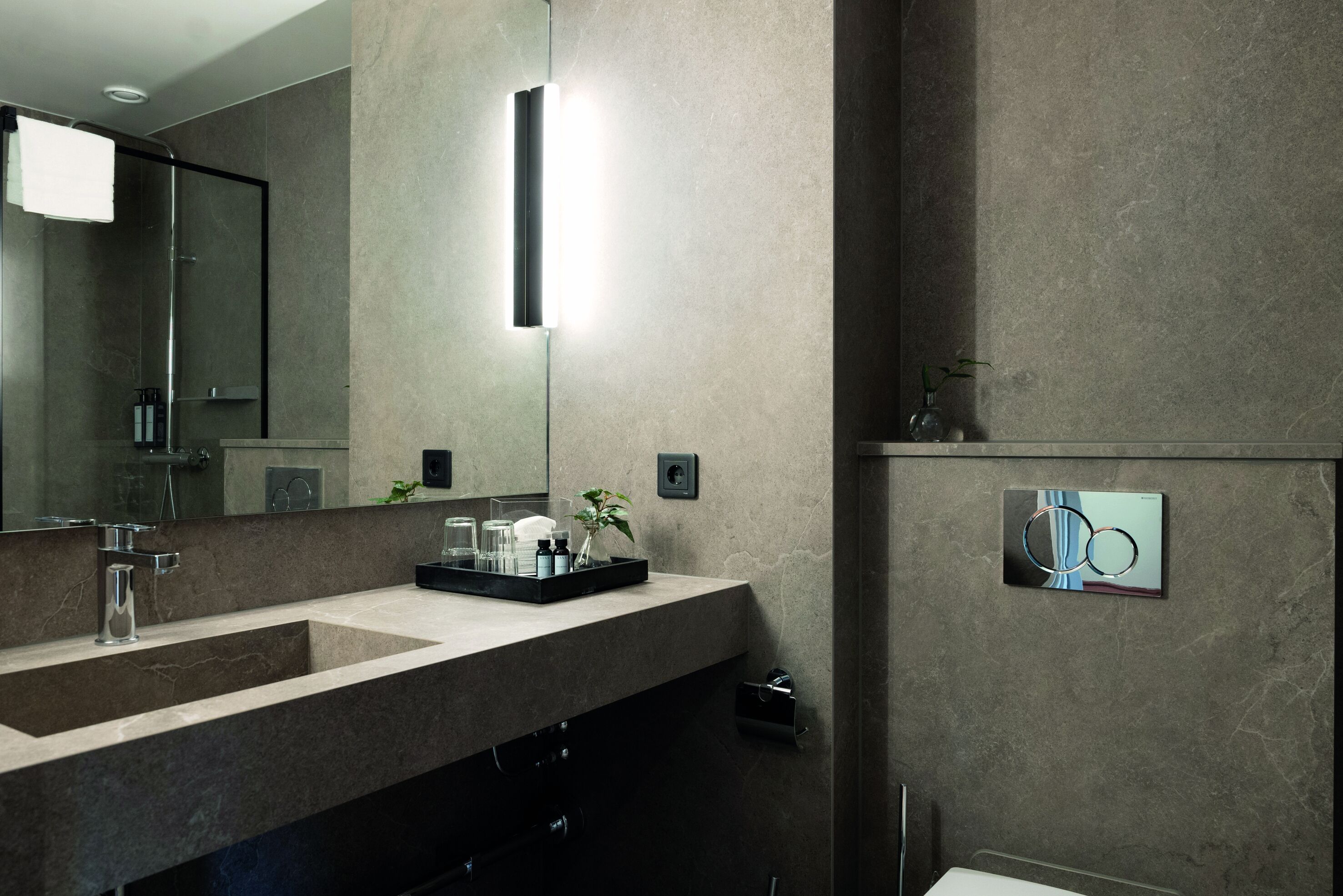 Un baño moderno con un espejo grande, dos lavabos, una ducha y una lámpara fijada a la pared.
