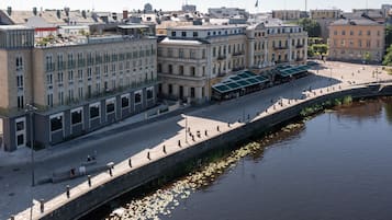 Un paseo fluvial bordeado por edificios históricos, una cafetería cubierta y un muro de piedra junto al agua.