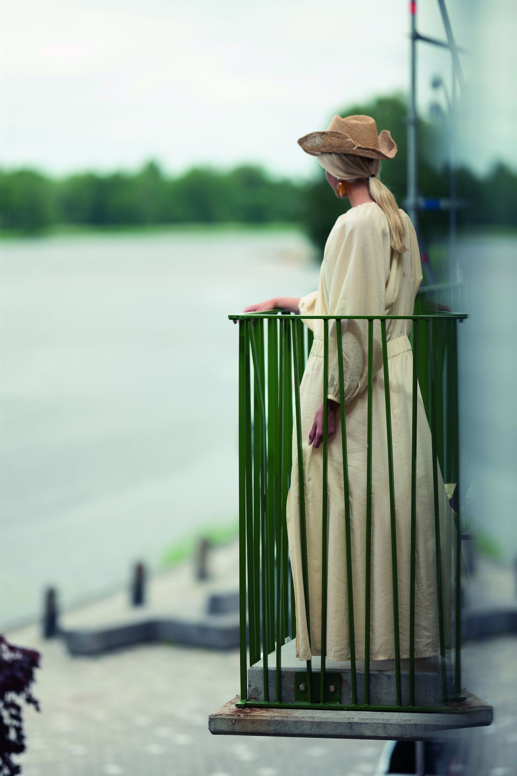 A person standing on a balcony with a railing, overlooking a body of water.