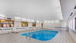 An indoor swimming pool with clear blue water, surrounded by white tiled flooring and walls.