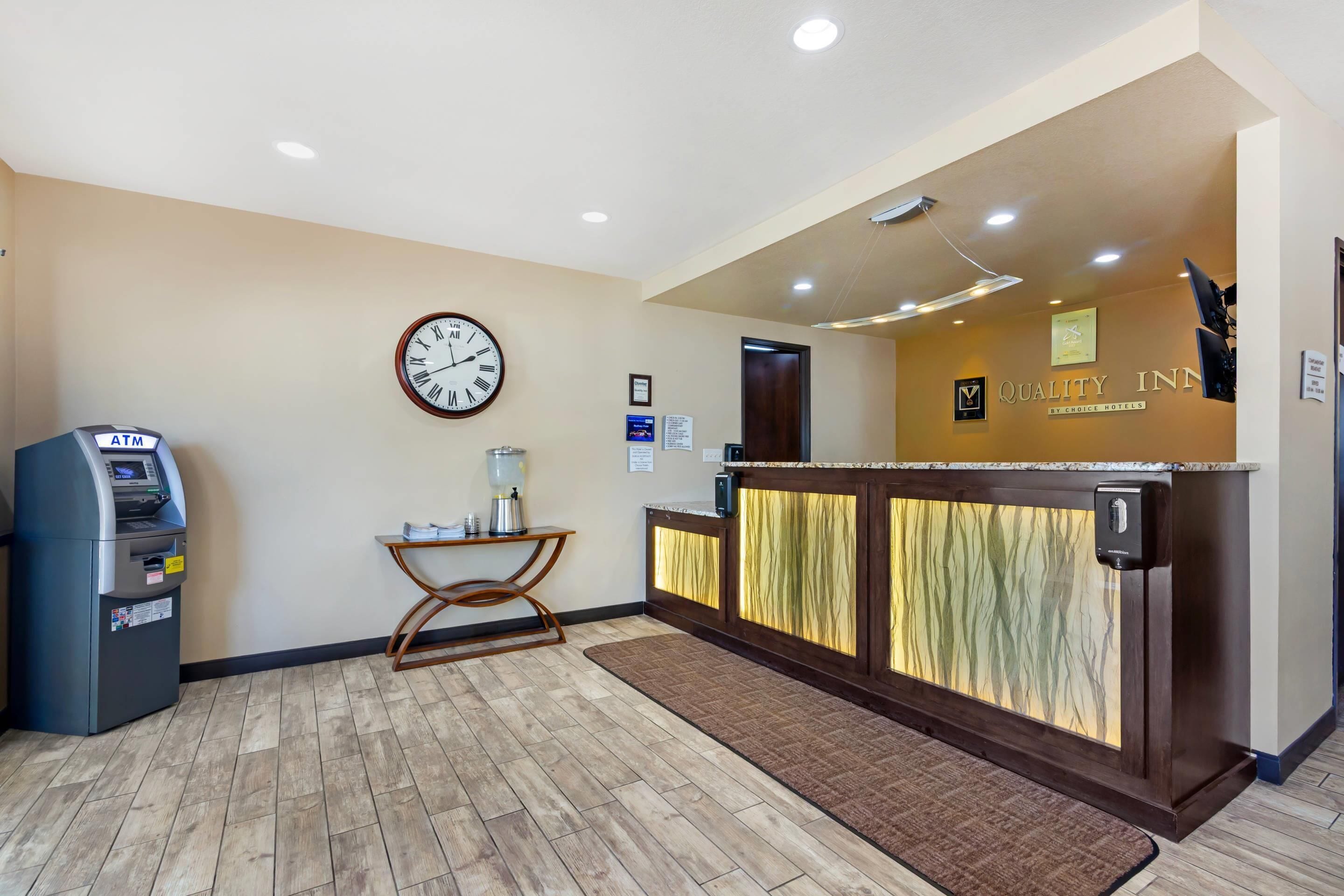 A reception area with a clock, an ATM, and a reception desk with a sign for Quality Inn by Choice Hotels.