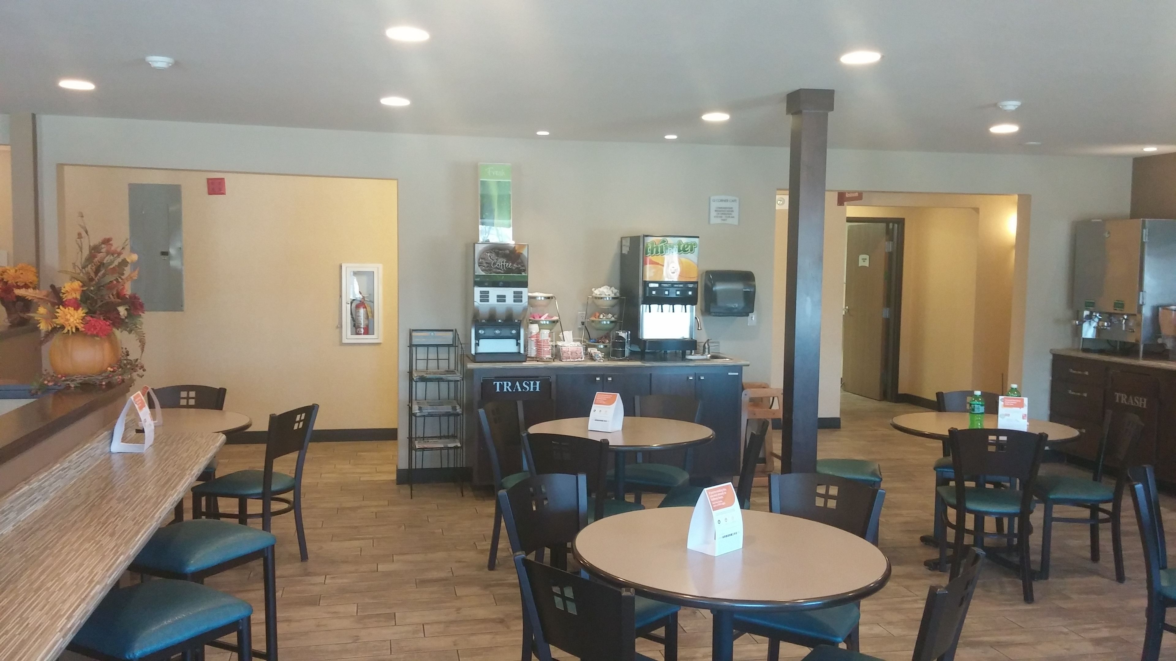 A restaurant with multiple tables and chairs, a coffee machine, and a trash bin labeled "TRASH".