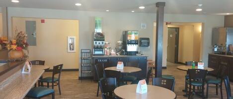 A restaurant with multiple tables and chairs, a coffee machine, and a trash bin labeled "TRASH".