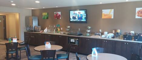 A hotel lobby with a reception area, seating, and a TV screen displaying a show.