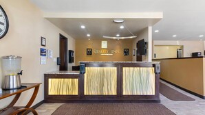 A reception desk with a sign reading "Quality Inn." There is a clock on the wall, a coffee machine, and a trash can.