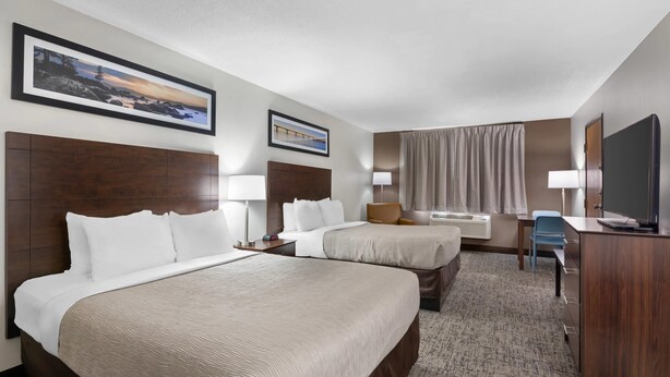 A hotel room with two beds, a desk, a chair, a TV, and a large window with curtains.