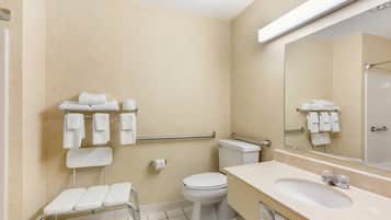 Un baño con inodoro, lavamanos, espejo y barra de apoyo.
