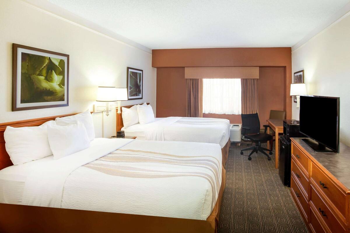 Habitación de hotel con dos camas, un escritorio, televisión y ventana con cortinas.