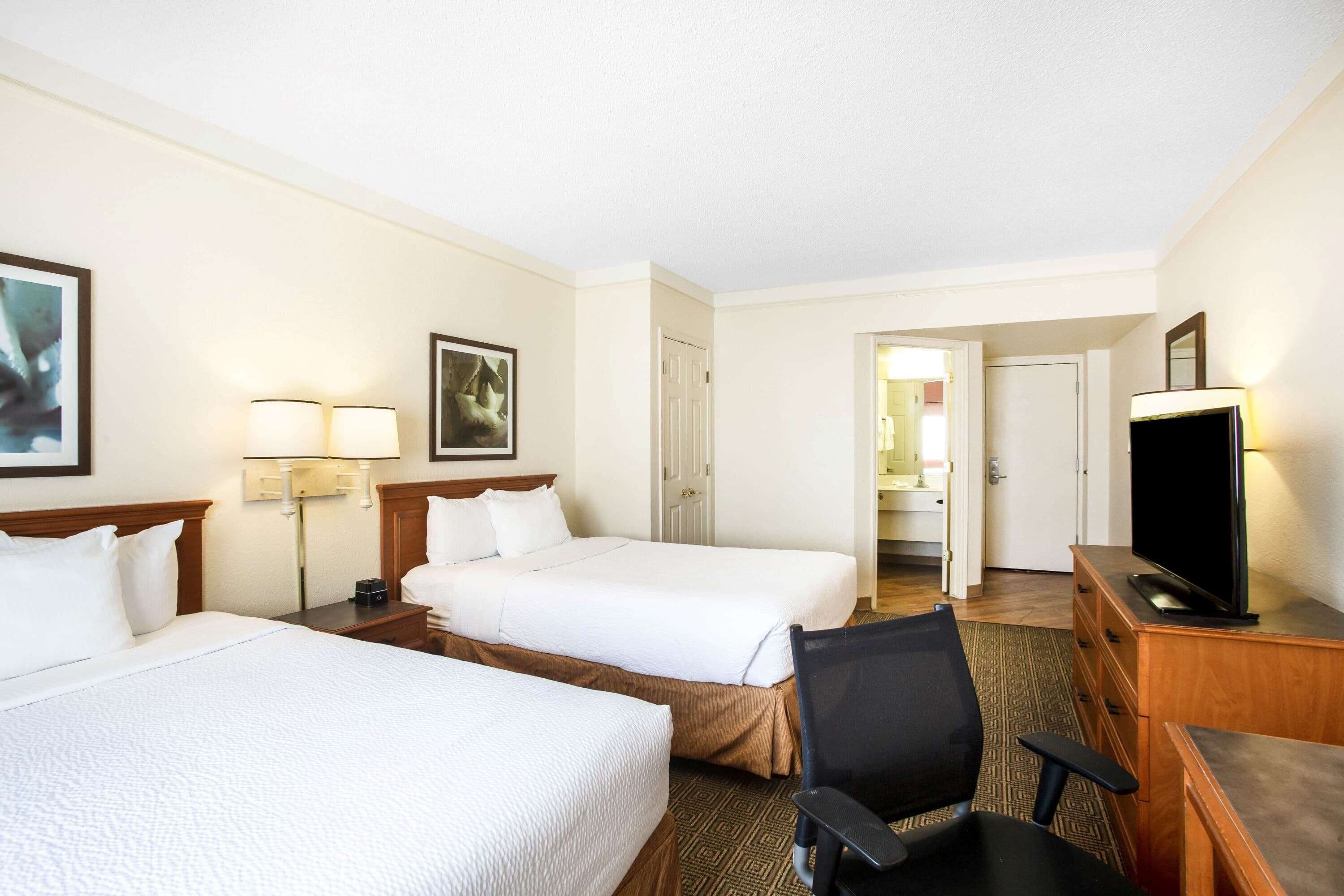 A hotel room with two beds, a desk with a television, and a chair.