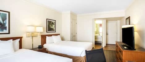 A hotel room with two beds, a desk with a television, and a chair.