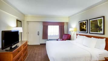 Una habitación de hotel con una cama grande, un televisor sobre una cómoda de madera, una silla roja y dos cuadros en la pared.
