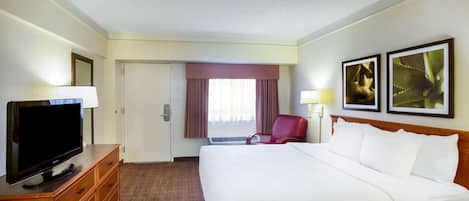 Ein Hotelzimmer mit einem großen Bett, einem Fernseher auf einer Holzkommode, einem roten Sessel und zwei gerahmten Bildern an der Wand.