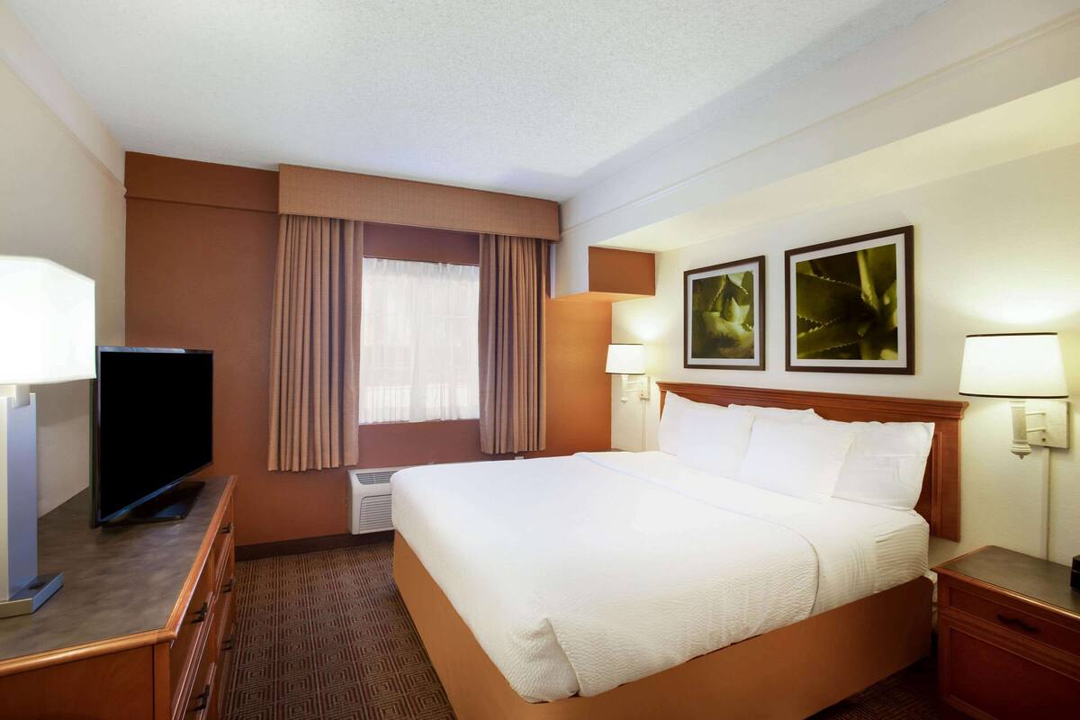 Habitación de hotel con una cama grande, un televisor de pantalla plana, un escritorio con lámpara y dos lámparas de pared.