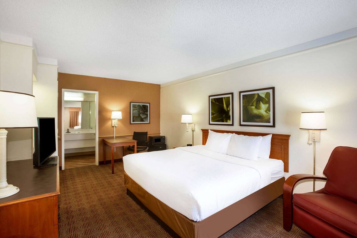 Habitación de hotel con una cama grande, un escritorio con silla, un televisor y dos lámparas de pared.