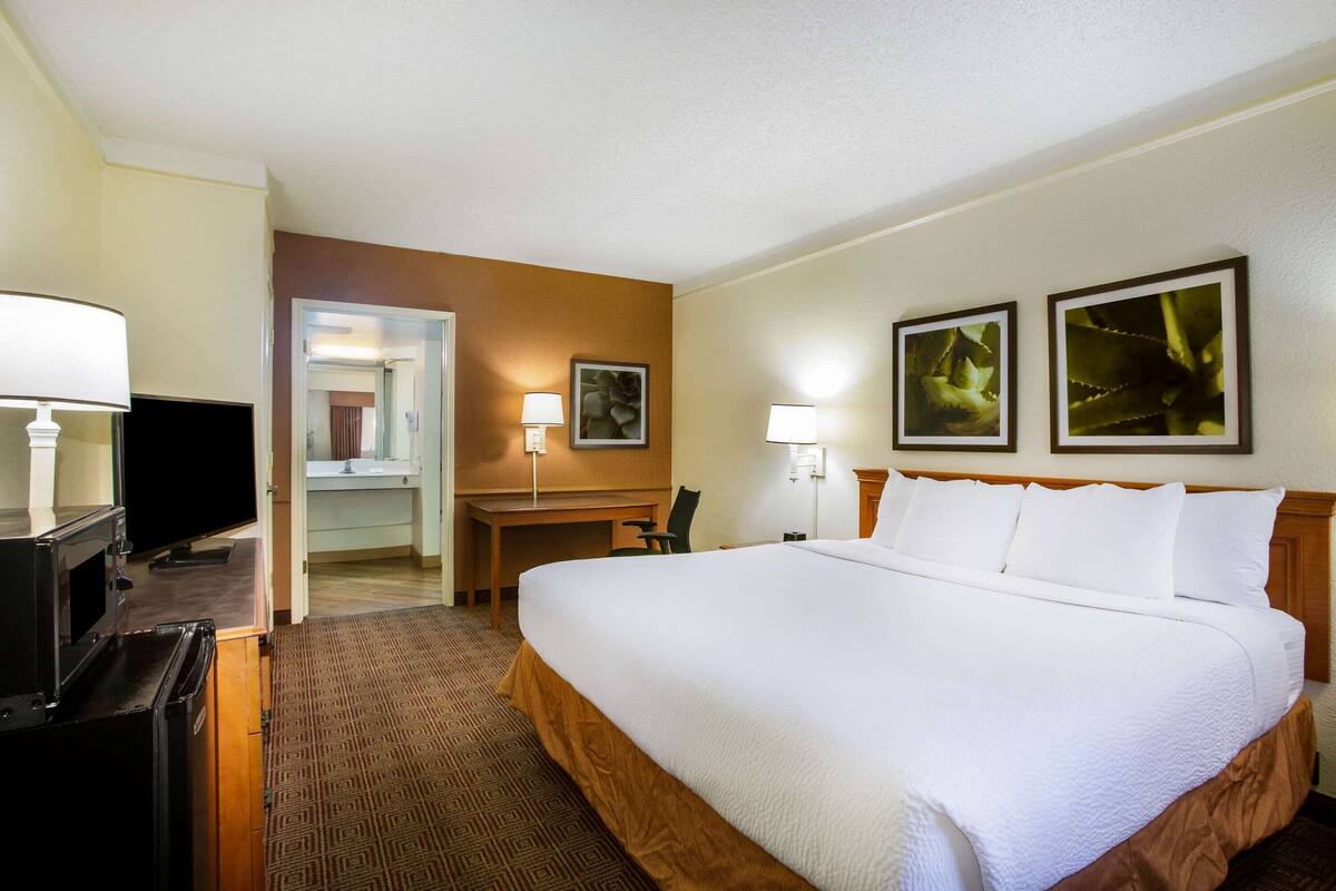 Una habitación de hotel con una cama grande, un escritorio, un televisor y dos lámparas fijadas a la pared.