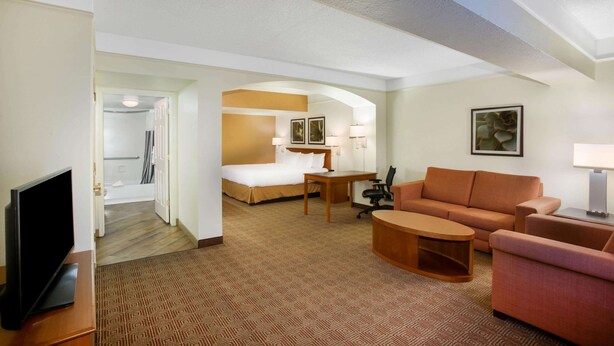 Een hotelkamer met een bed, een bureau, een bank, een televisie en een badkamer die door een geopende deur zichtbaar is.