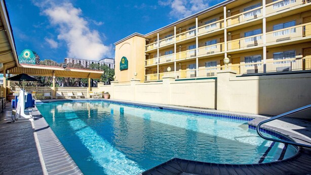 A hotel with a swimming pool, a covered area with umbrellas, and a building with balconies.