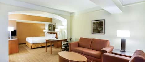A hotel room with a bed, a sofa, a coffee table, a desk, and a lamp.