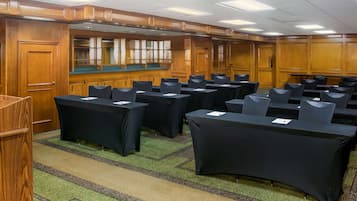 A conference room with multiple tables and chairs, wooden paneling, and a carpeted floor.