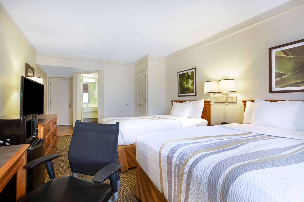 Habitación de hotel con dos camas, un escritorio con televisor, una silla y una lámpara.