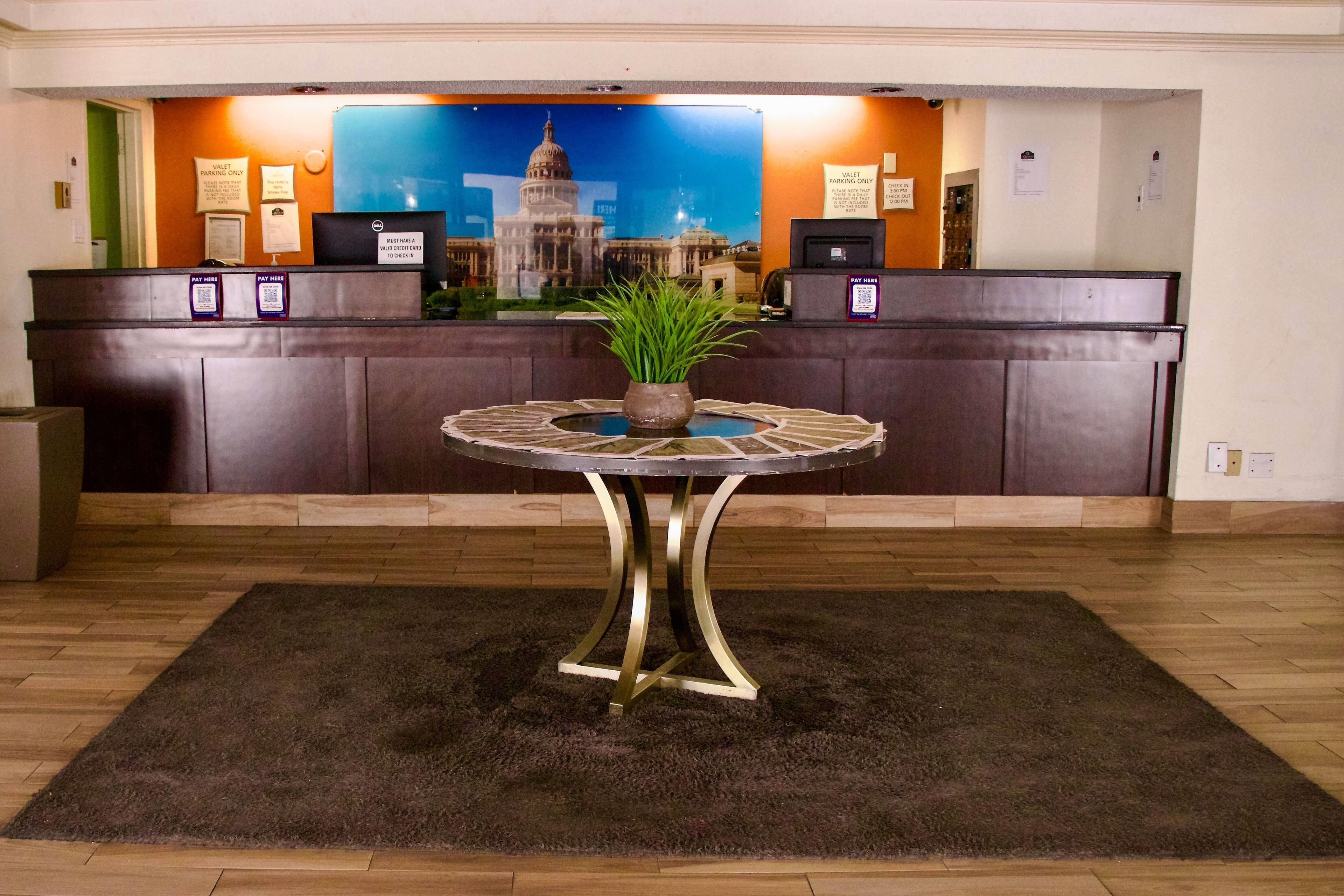 A reception desk with a check-in counter, a potted plant, and a round table in the foreground.