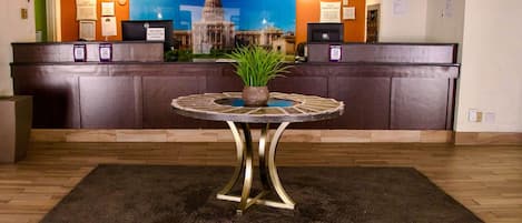 Un comptoir d’accueil avec un guichet d’enregistrement, une plante en pot et une table ronde au premier plan.