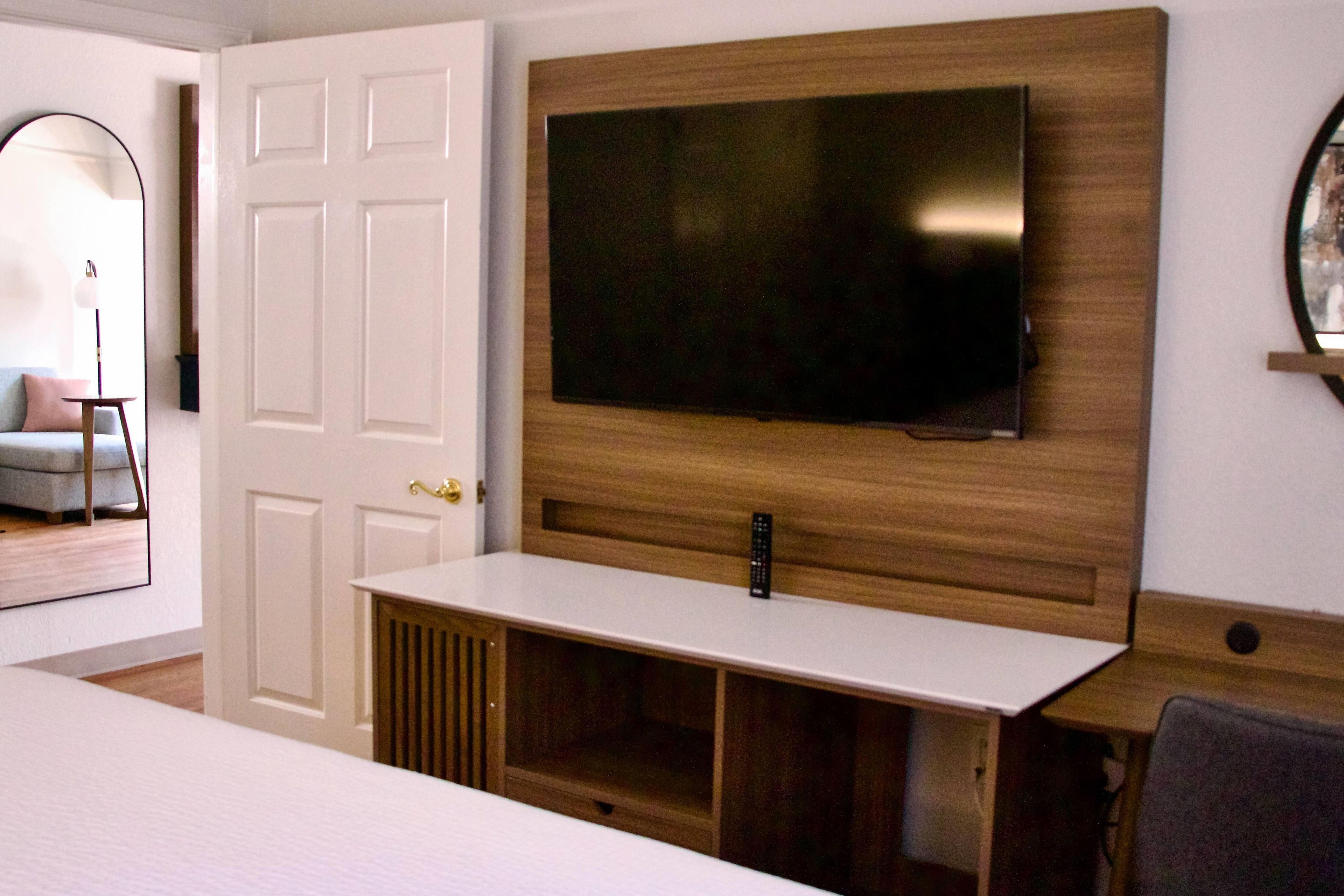 Een kamer met een flatscreen televisie aan een houten wand, een witte console tafel en een deur met een witte omlijsting.