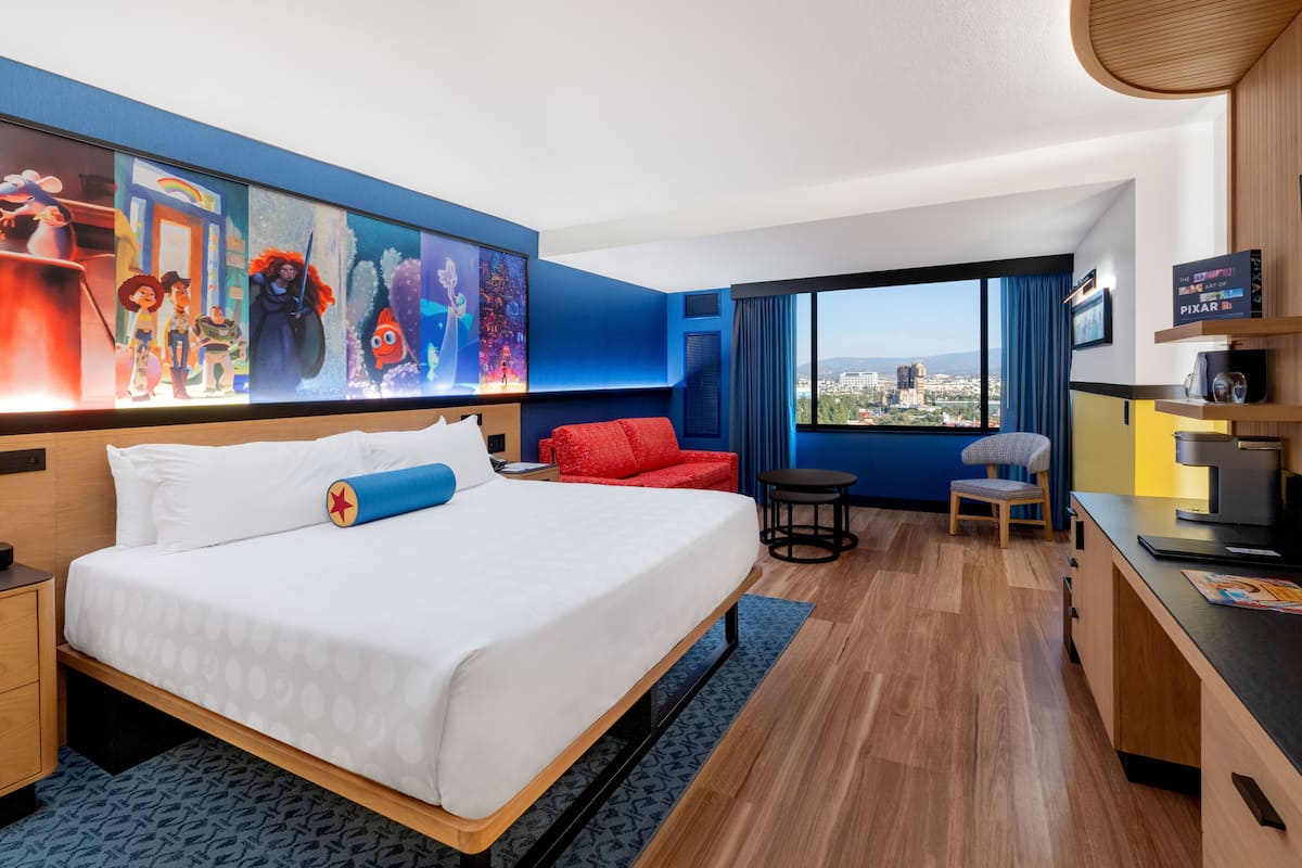 Ein Hotelzimmer mit einem großen Bett, einem roten Sofa, einem Schreibtisch mit Stuhl, einem Fernseher und Blick auf die Stadt durch das Fenster.