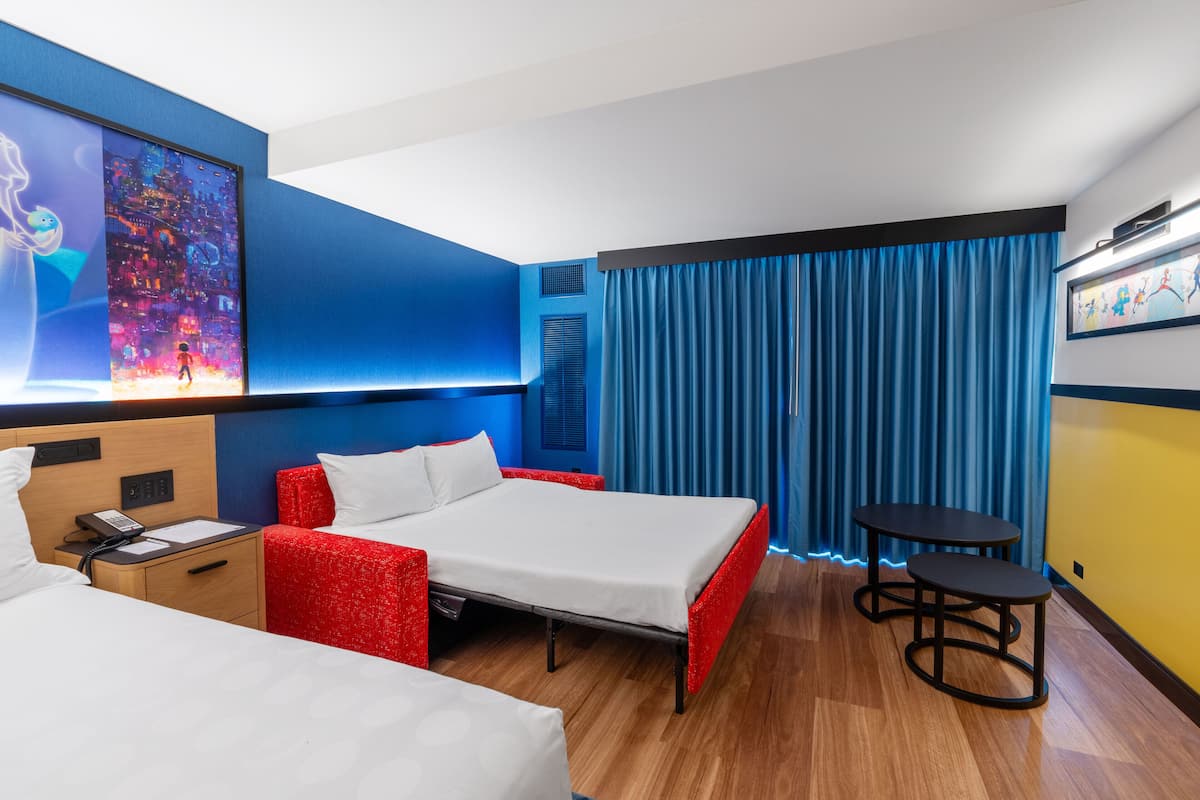 Ein Hotelzimmer mit einem Bett, einem Schreibtisch mit Telefon, einem kleinen Tisch und einem großen Poster an der Wand.