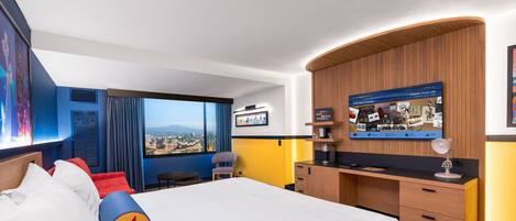 A hotel room with a large bed, a desk, a TV, and a view of the city.
