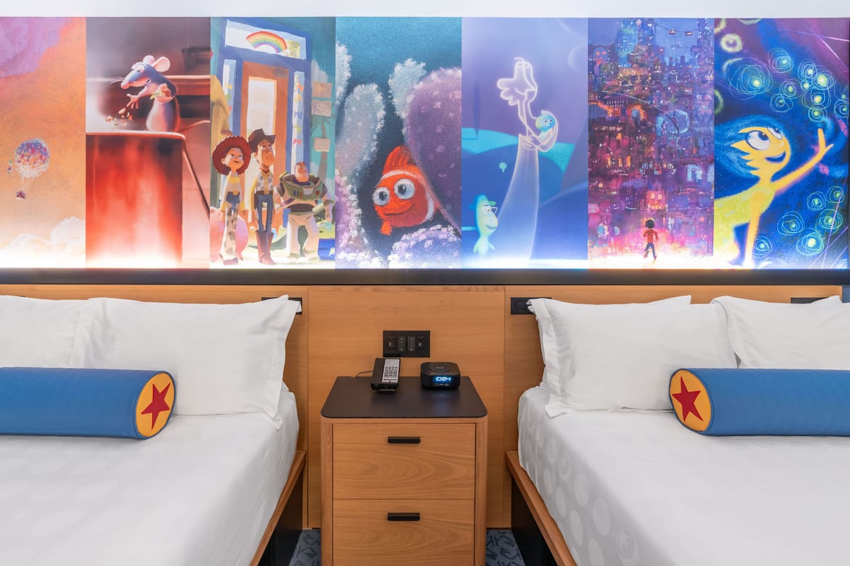 Ein Hotelzimmer mit zwei Betten, einem Nachttisch und Wandbild mit Zeichentrickfiguren.