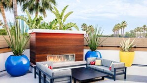 An outdoor seating area with a modern fire pit, large potted plants, and a view of palm trees. - Pixar Place Hotel (Anaheim)