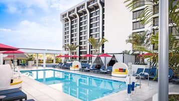 A swimming pool area with lounge chairs and umbrellas, surrounded by a multi-story building.