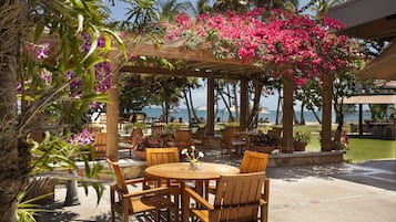 Eine Außenpatio-Terrasse mit Holzmöbeln, einem mit rosa Blüten bepflanzten Pergola und Meerblick.