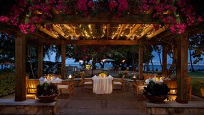 A covered outdoor dining area with wooden tables and chairs, string lights, and a view of the ocean. - Copamarina Beach Resort & Spa (Guanica)