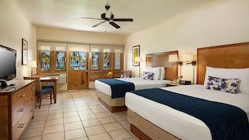 A hotel room with two beds, a desk, a television, and a ceiling fan.