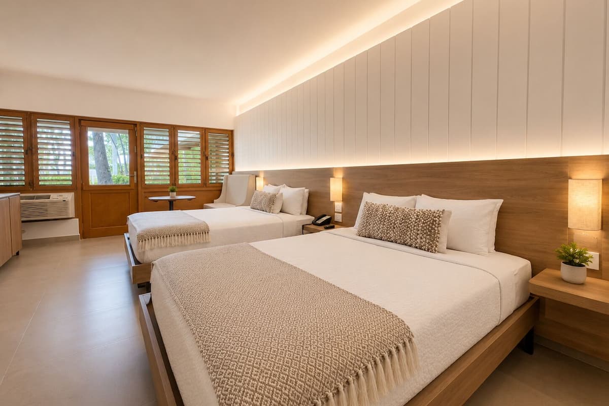 Ein modernes Hotelzimmer mit zwei Betten, einem Holz-Kopfteil, Nachttischlampen, einem kleinen Tisch und einem Fenster mit Jalousien.
